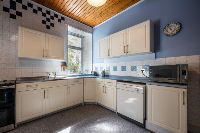 Country-style kitchen with white cabinetry, wooden ceiling panelling and white backsplash.