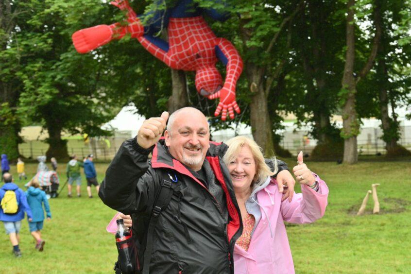 Couple smiles for pictures as giant Spiderman hangs from tree in the background.