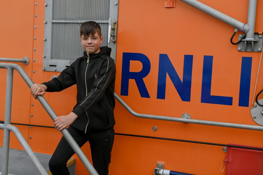 Young boy standing next to RNLI signage.