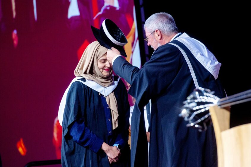 A graduate student is tapped on the head with a cap as she graduates.