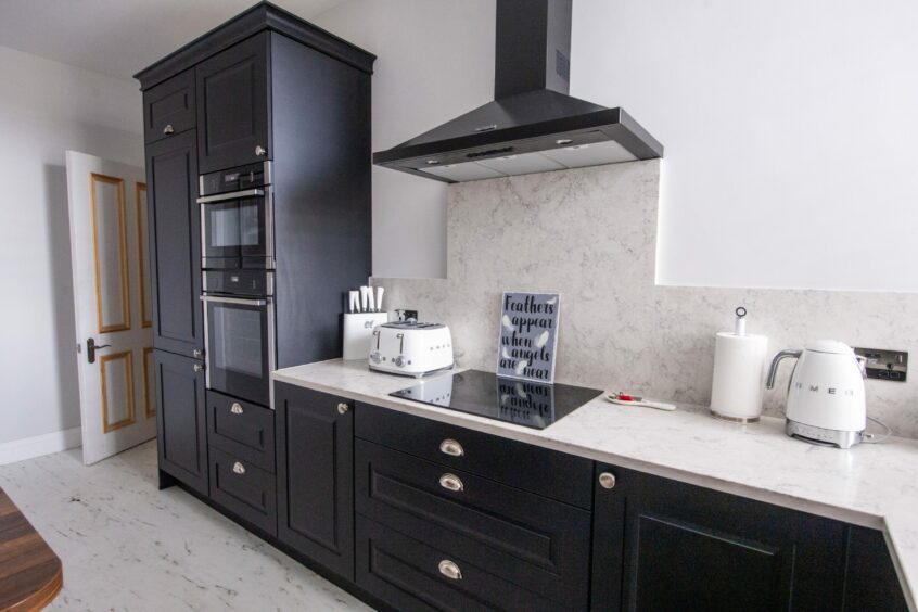 Modern kitchen with matt black cabinetry and light marble countertops and backsplash.