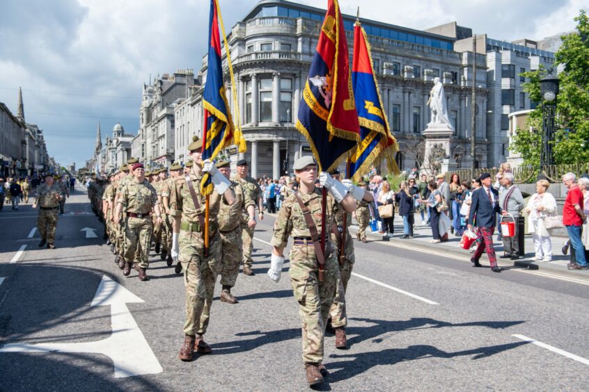 Military personnel marching with flags down the centre of Union Street.