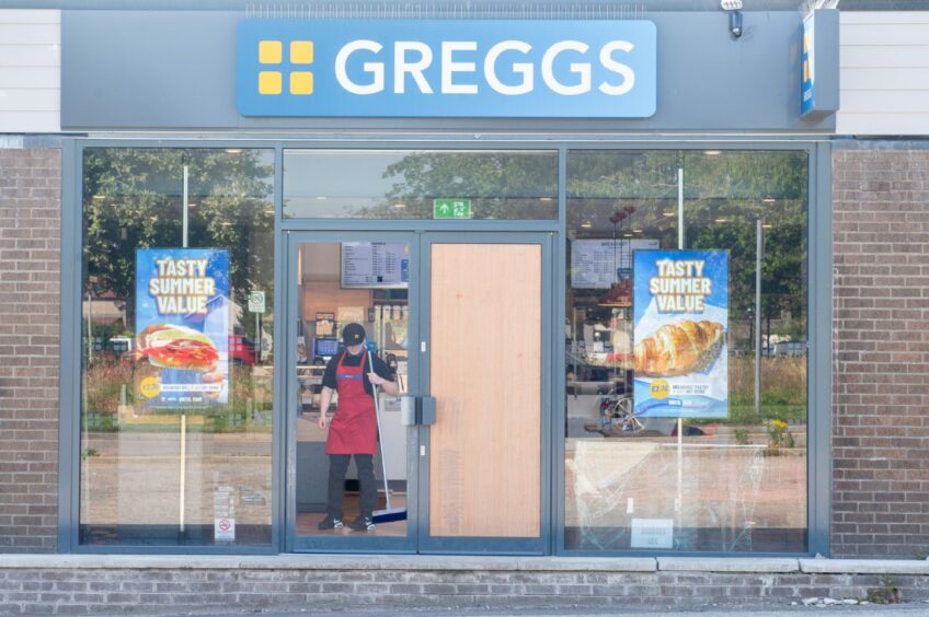 Outside of Greggs in Dyce, with a worker standing with a brush.