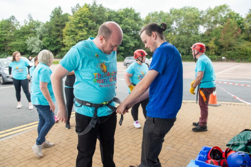 A man wearing an Archie Foundation t-shirt putting his abseiling safety gear on 