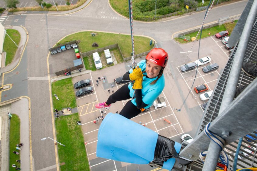 A woman abseiling in the forefront with people and cars on the ground 