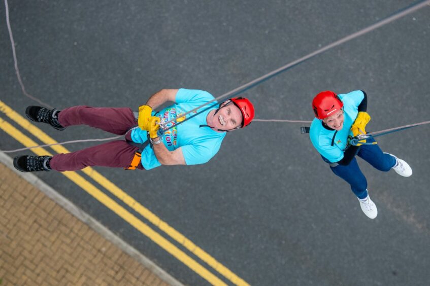 Jim Souter and Carole Duncan look up at the camera as they abseil 