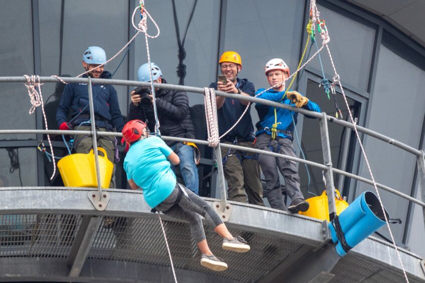 Four men on the tower look down on a woman starting her abseil