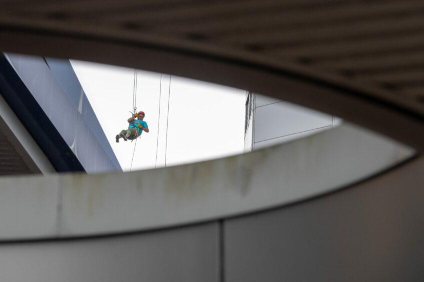 A woman can be seen abseiling through a gap in the building 