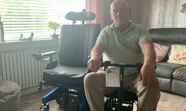 Malcolm Ritchie sitting in the scooter he used on the Loganair flight with wheelchair next to him.
