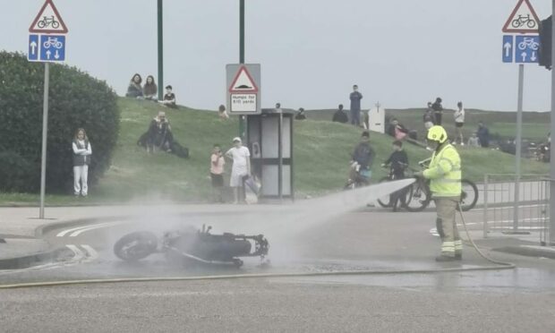 One fireman hosing down a motorbike with members of the public behind.