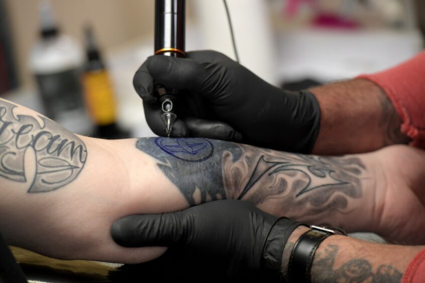 A tattoo artist at work tattooing someone's arm