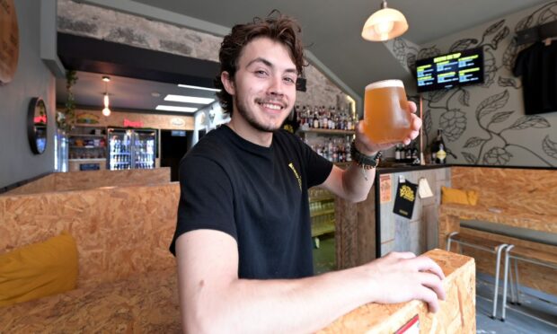 Calum smiling in his bar Against The Grain with a glass full of beer in his hand.