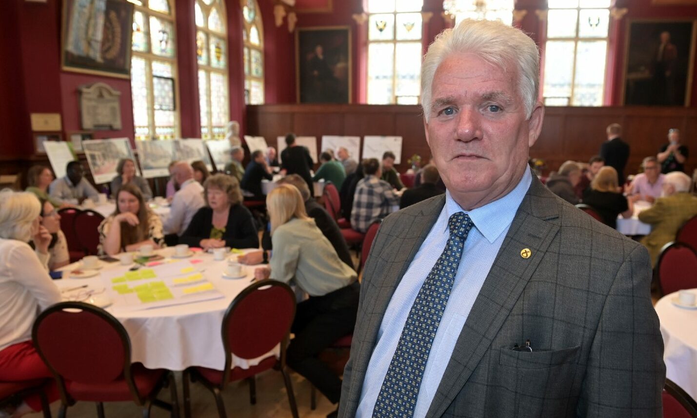 Councillor Ian Brown at a meeting in Inverness Town House with people behind. 