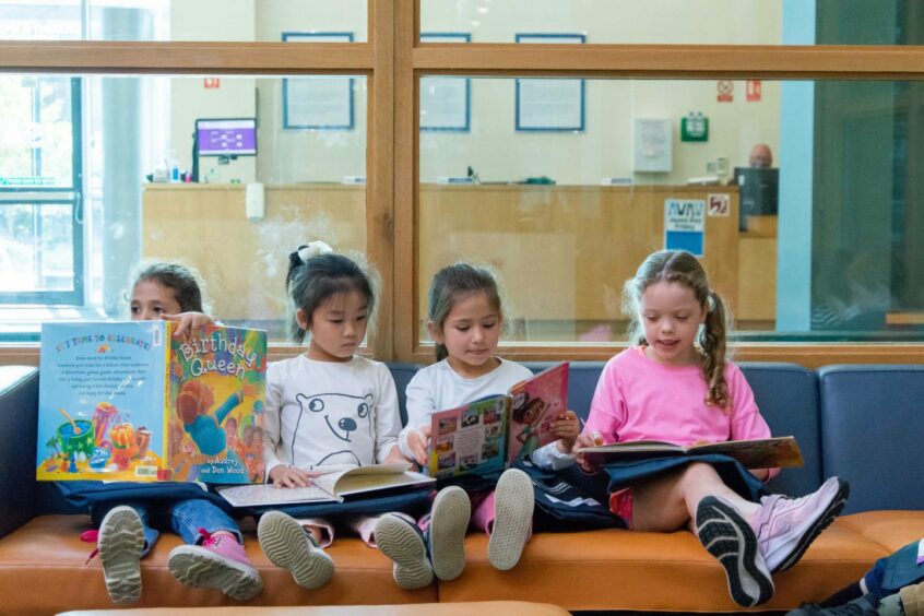 Young students at ISA pre-school sat reading books on a bench.