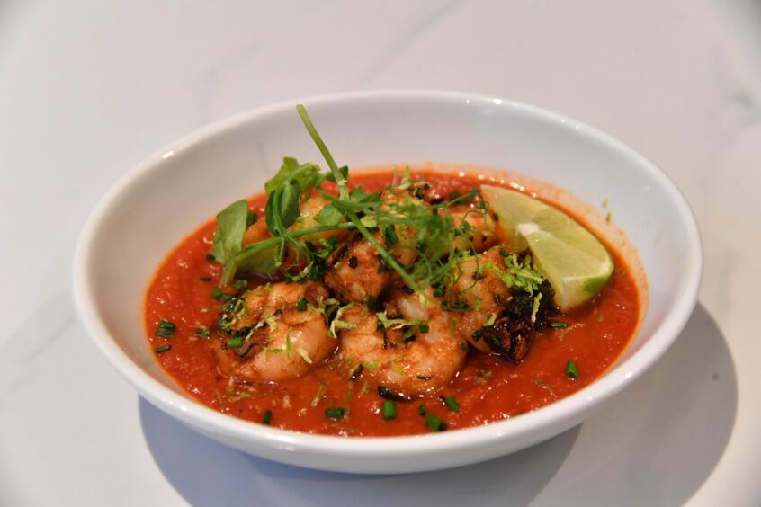The gambas dish featuring prawns in a tomato sauce, garnished with chives, coriander and a lemon wedge.