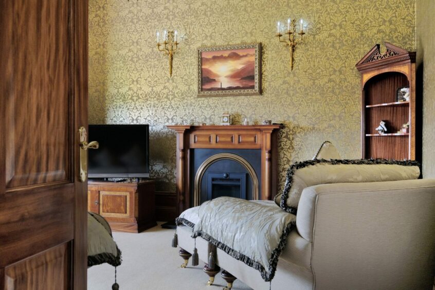 A period-looking sitting room with a chaise, faux candle wall light