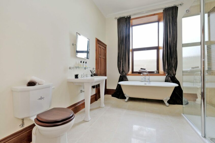 A bathroom in the property, with a fairly large amount of tiled floor space, a walk-in glass shower cubical and a free standing bath next to a frosted window