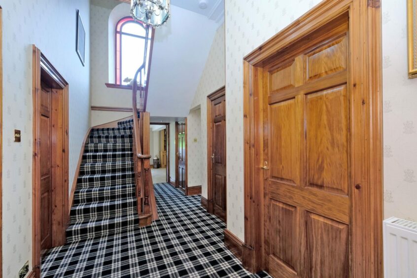 a hallway of the former Banff manse, with a set of stairs, wooden doors and plaid carpet
