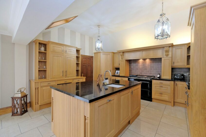 The kitchen in the former banff manse, with wooden cupboards, black counters and a large kitchen islands with a sink in the middle of the room