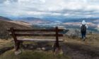 Woman with backpack stood next to a bench over looking the Nevis Range.