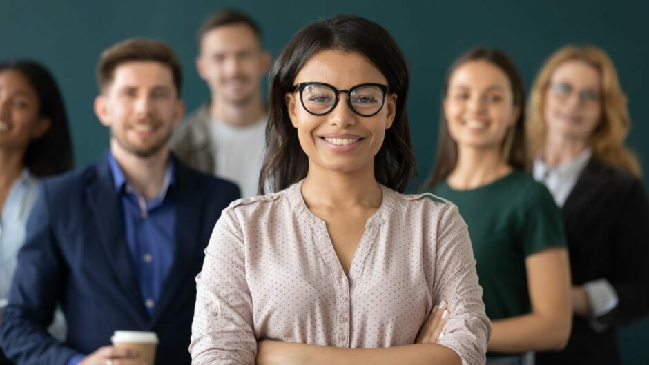 Confident business woman standing in front of team, smiling at camera. 