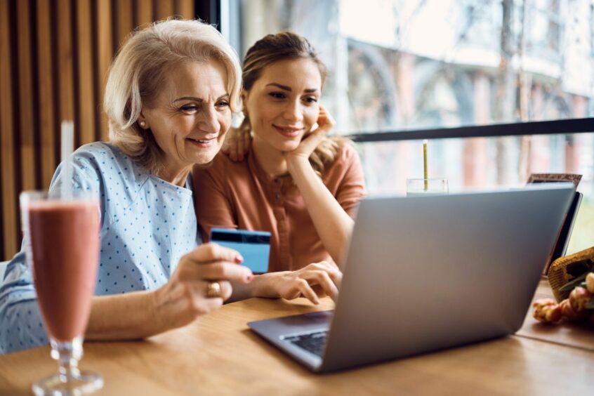 Happy mature mother using credit card and laptop with her daughter .