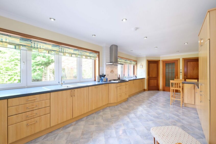 The kitchen in the Bieldside house, with light wooden cupboards, dark grey countertops and light grey floor tiles
