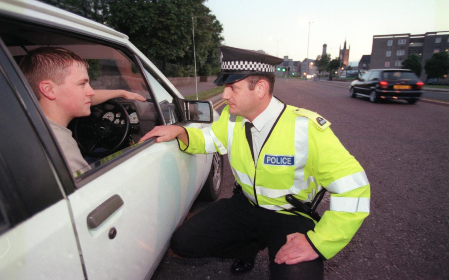 A policeman kneeling down to talk to a man in a car with his window down