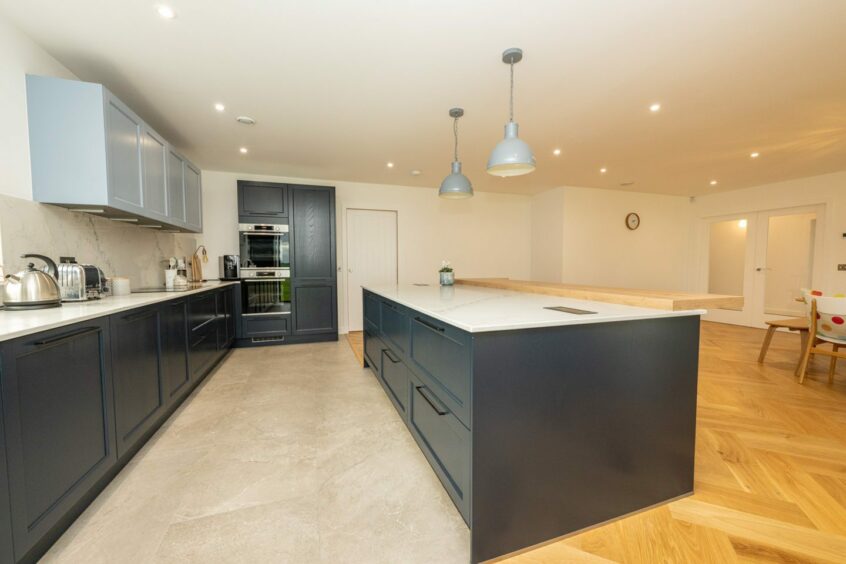 Spacious kitchen and dining area in the house for sale in Udny, featuring navy cupboards with white countertops and a large island.