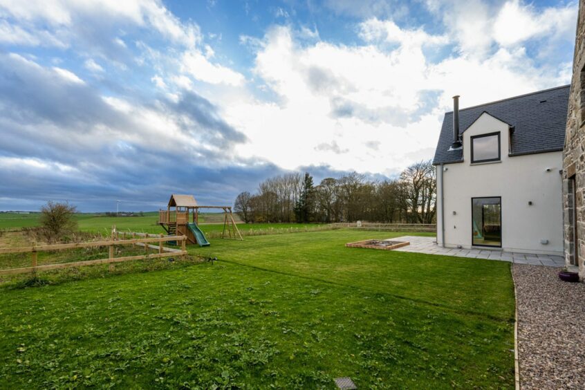 The garden of the Undy property in the Aberdeenshire countryside. There's a stone patio and a large area of grass with a wooden playset with a swing set and slide