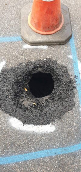 An orange cone pictured beside a large black sinkhole.