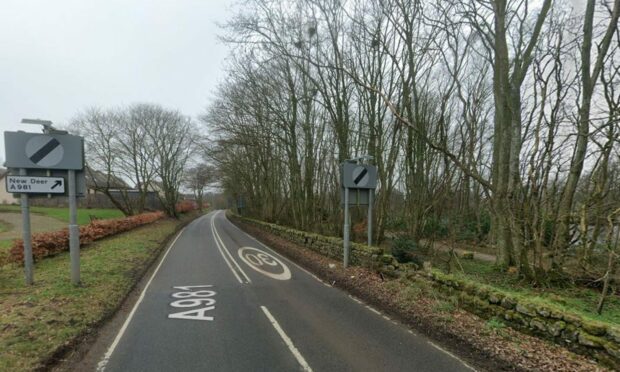 A view of the A981 leaving Strichen, lined with trees and houses.