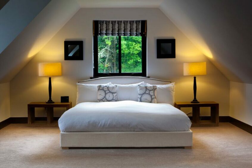 bed positioned in the middle of a cosy room with illuminated lamps on the bedside tables. there's a window above the bed with a view of a lush garden