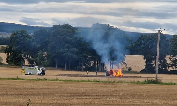 Hay bales on fire in a field with a fire engine stationed nearby.