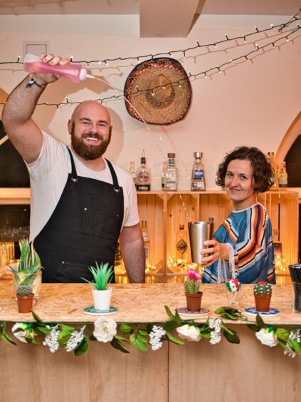Man and woman standing next to each other making cocktails.