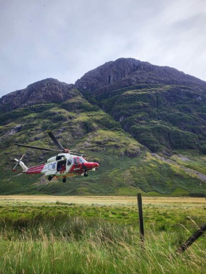 The red and white coastguard rescue helicopter from Prestwick hovers above the group close to a Highland peak.