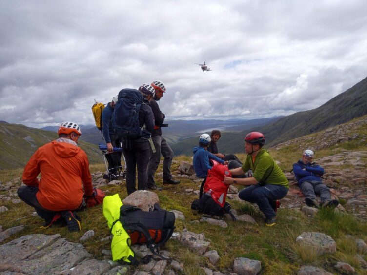 Members of Glencoe Mountain Rescue Team sit down for a rest as the coastguard helicopter flies above.