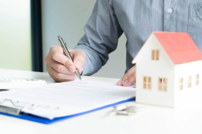 Someone signing a document with a model house on the table next to them 