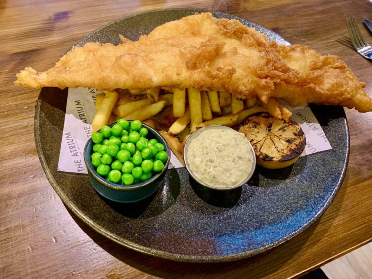 Fish and chips served with a dish of garden peas, tartar sauce and a slice of lemon