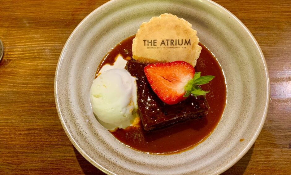 Sticky toffee pudding with half a strawberry on top, a wafer and a scoop of vanilla ice cream