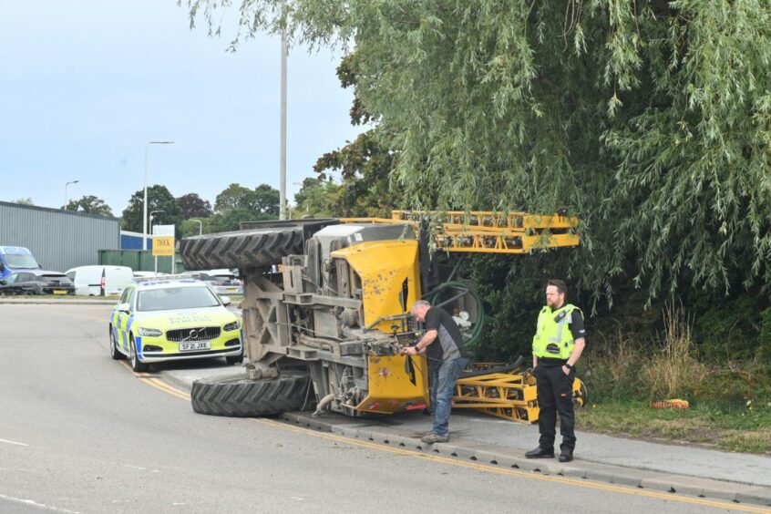 Police at the scene as the overturned tractor blocks a pavement on the A96 road through Elgin.
