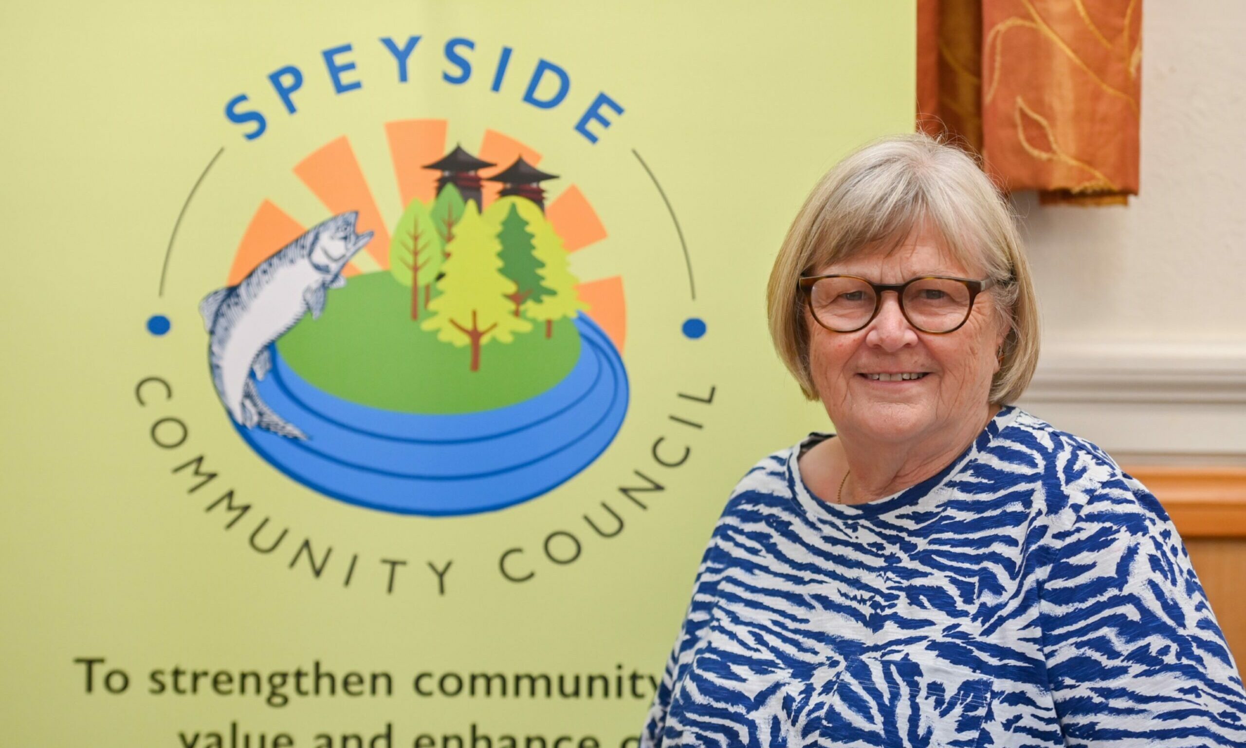 Marion Ross standing in front of a Speyside Community Council posted. 