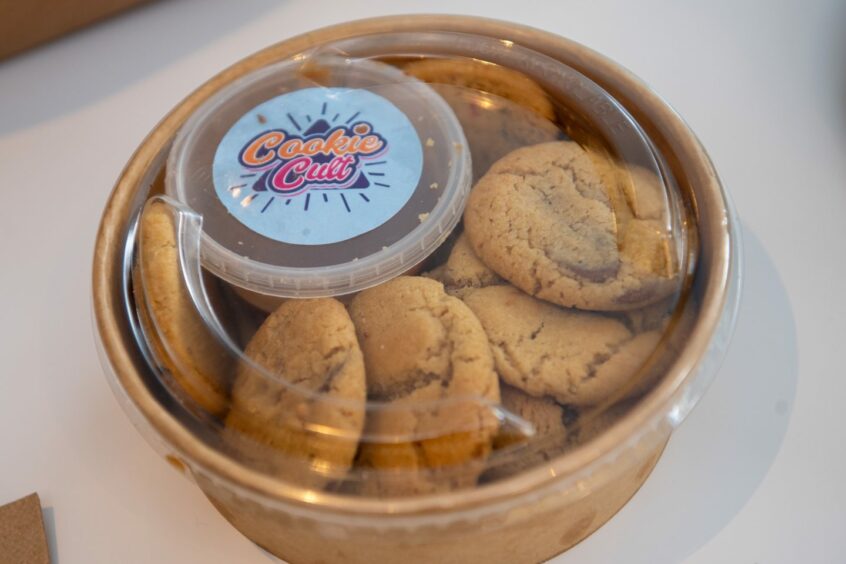 A takeaway container of chocolate chip cookies with a pot of sauce to dip them in