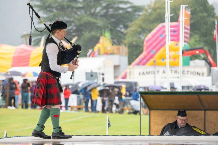 A lone piper, wearing a red kilt, performs on stage in a solo piping competition.