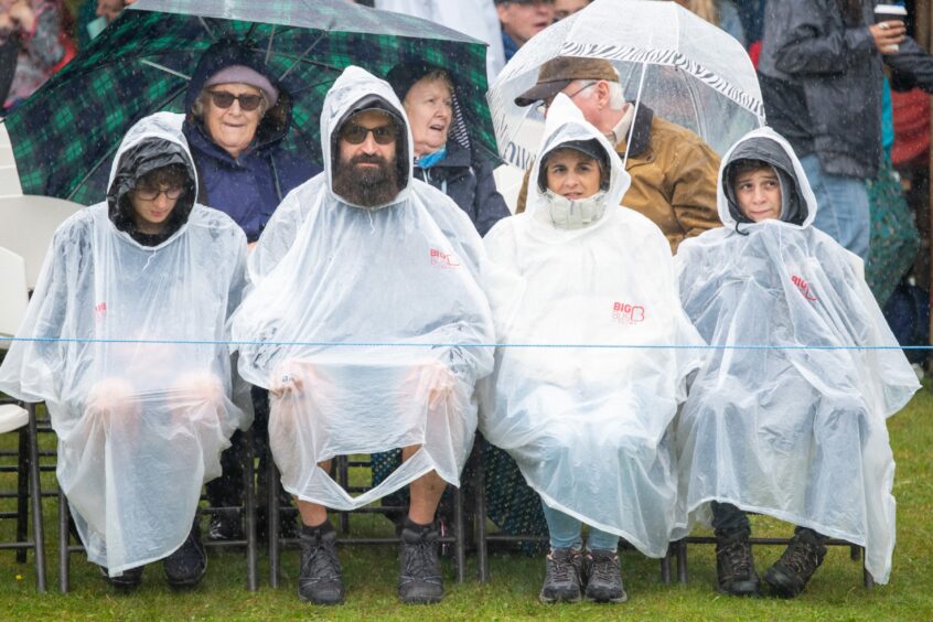 Four people sat in white ponchos watch the action at Aboyne Games 2023.