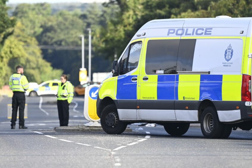 Police officer standing beside police van, with car in background.