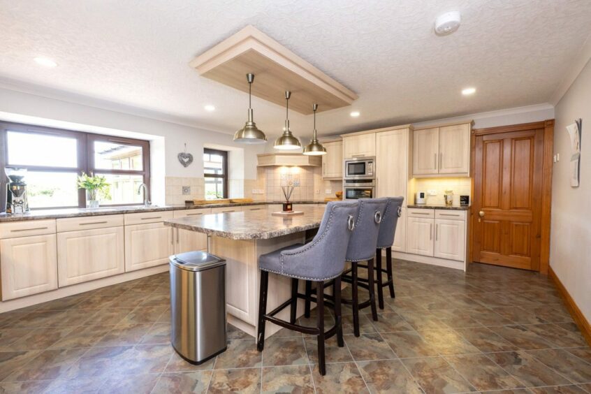 The kitchen in the Ellon property, with pale wooden cupboard, a kitchen island and three breakfast bar stools