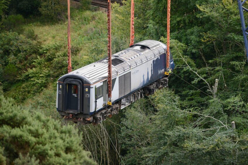 A rail carriage is suspended in the air as its removed by crane from the site. 