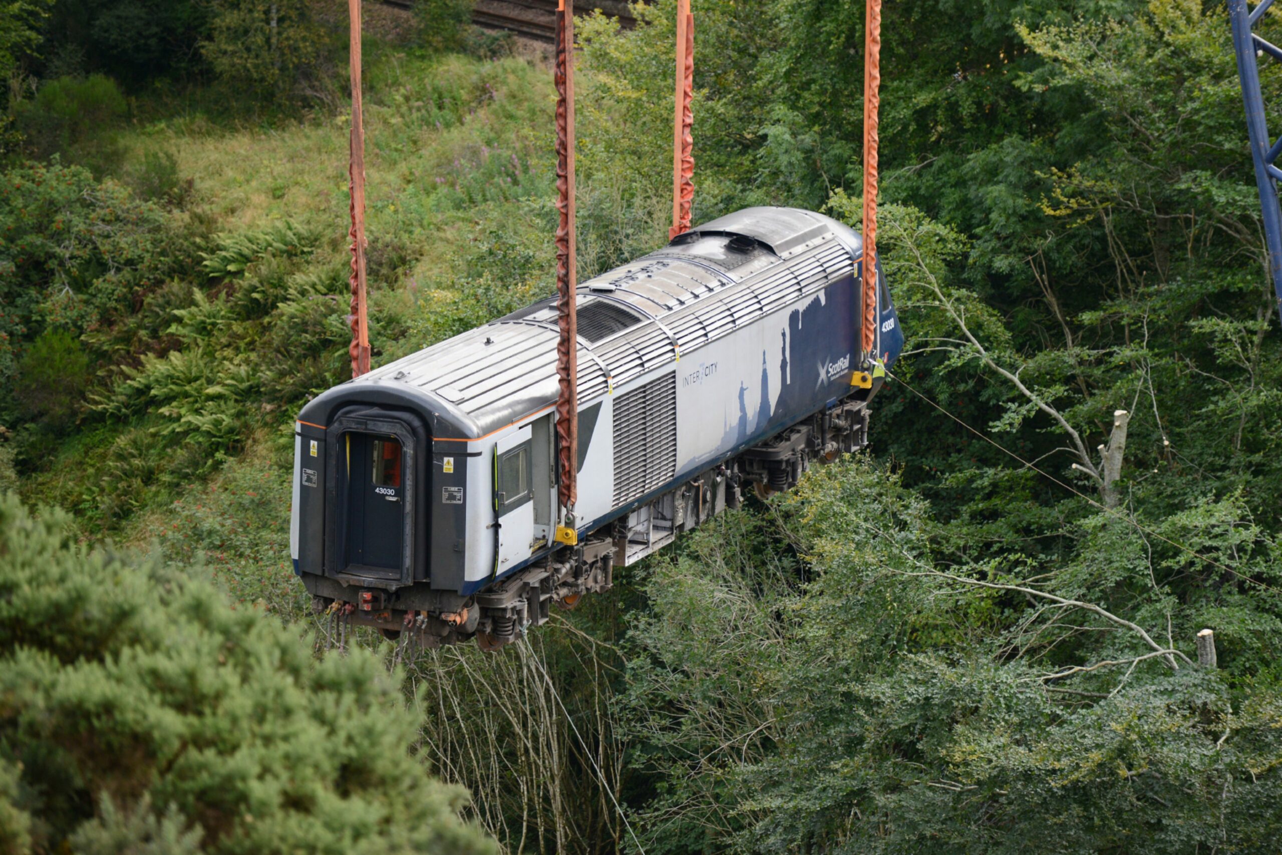 A rail carriage is suspended in the air as its removed by crane from the site.