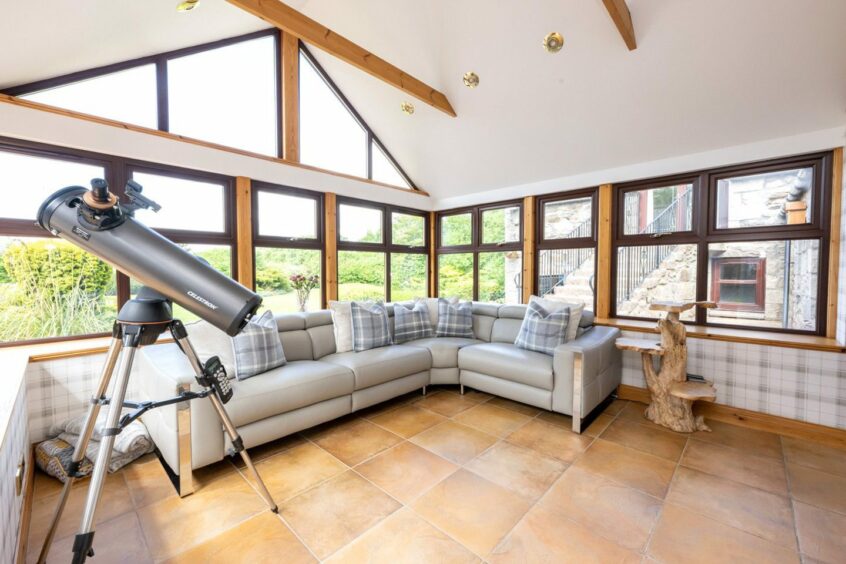 The sun room in the home, featuring an L-shaped sofa, a statement wooden end table and a large telescope